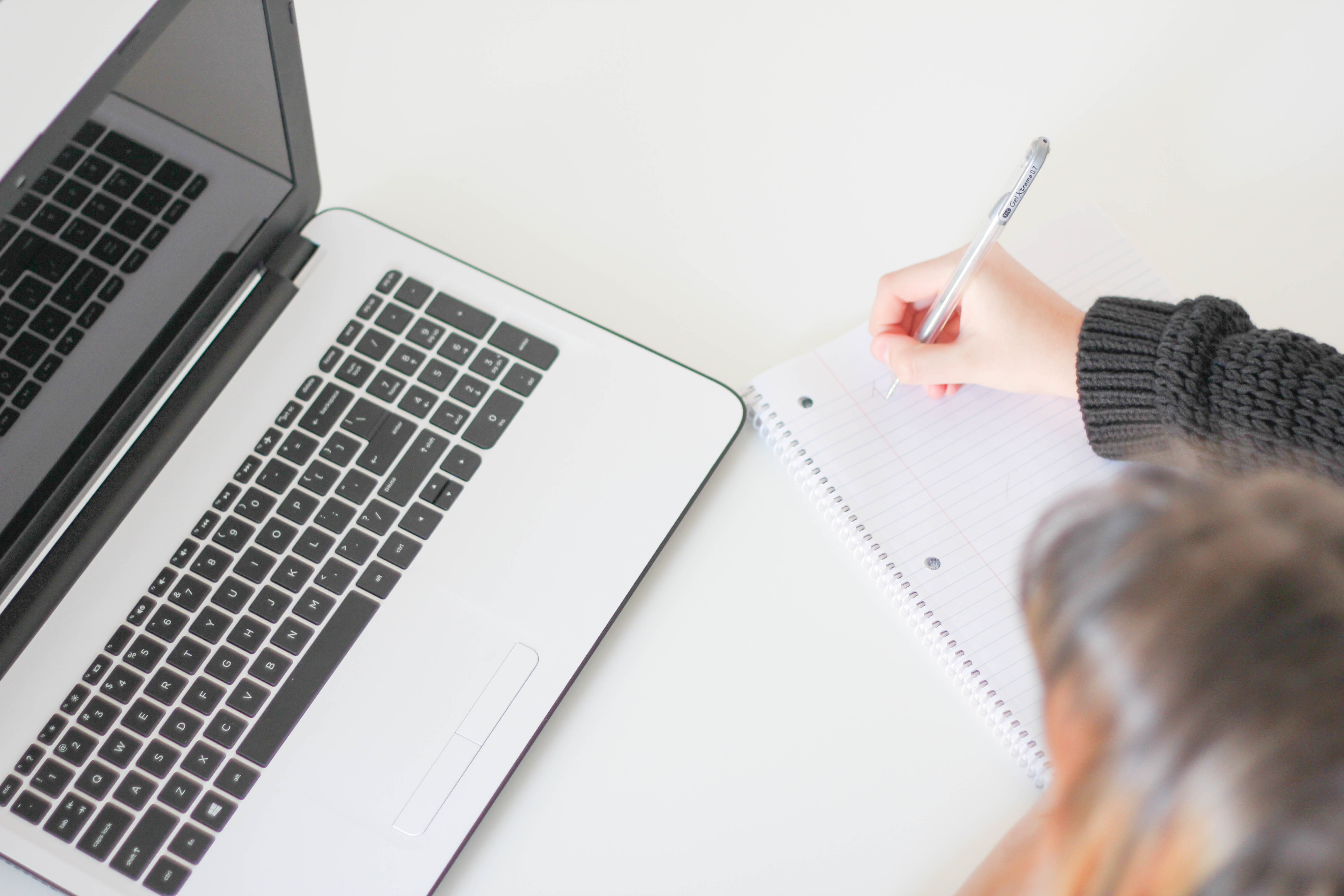 woman writing in notebook with laptop